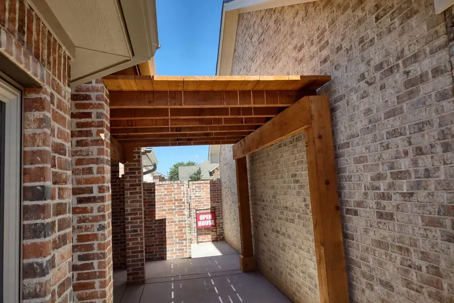 A wooden pergola is attached to the side of a brick building.