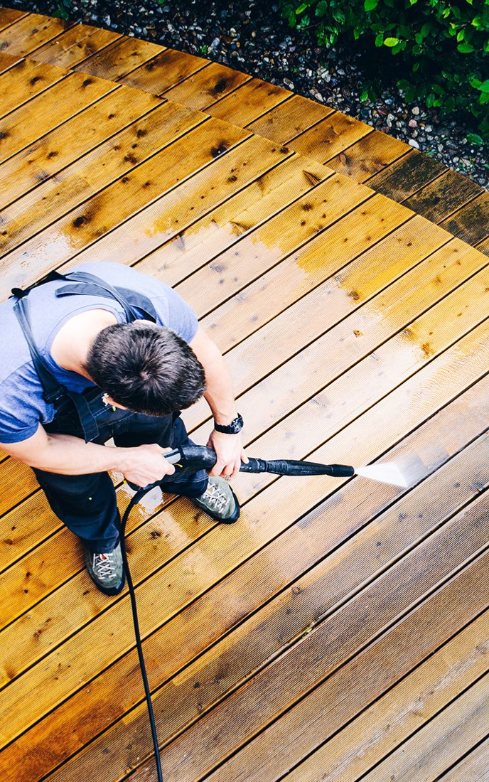 Man power washing wooden deck; light brown boards being cleaned with water.