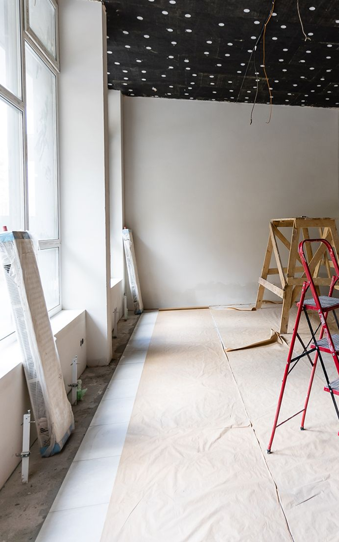 Interior construction: bare walls, covered floor, ladder, wood, window.