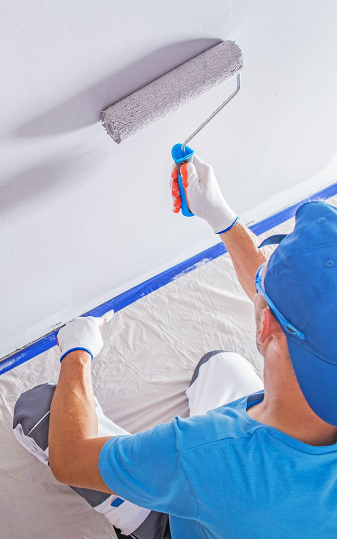 Person in blue painting a white ceiling with a gray paint roller.