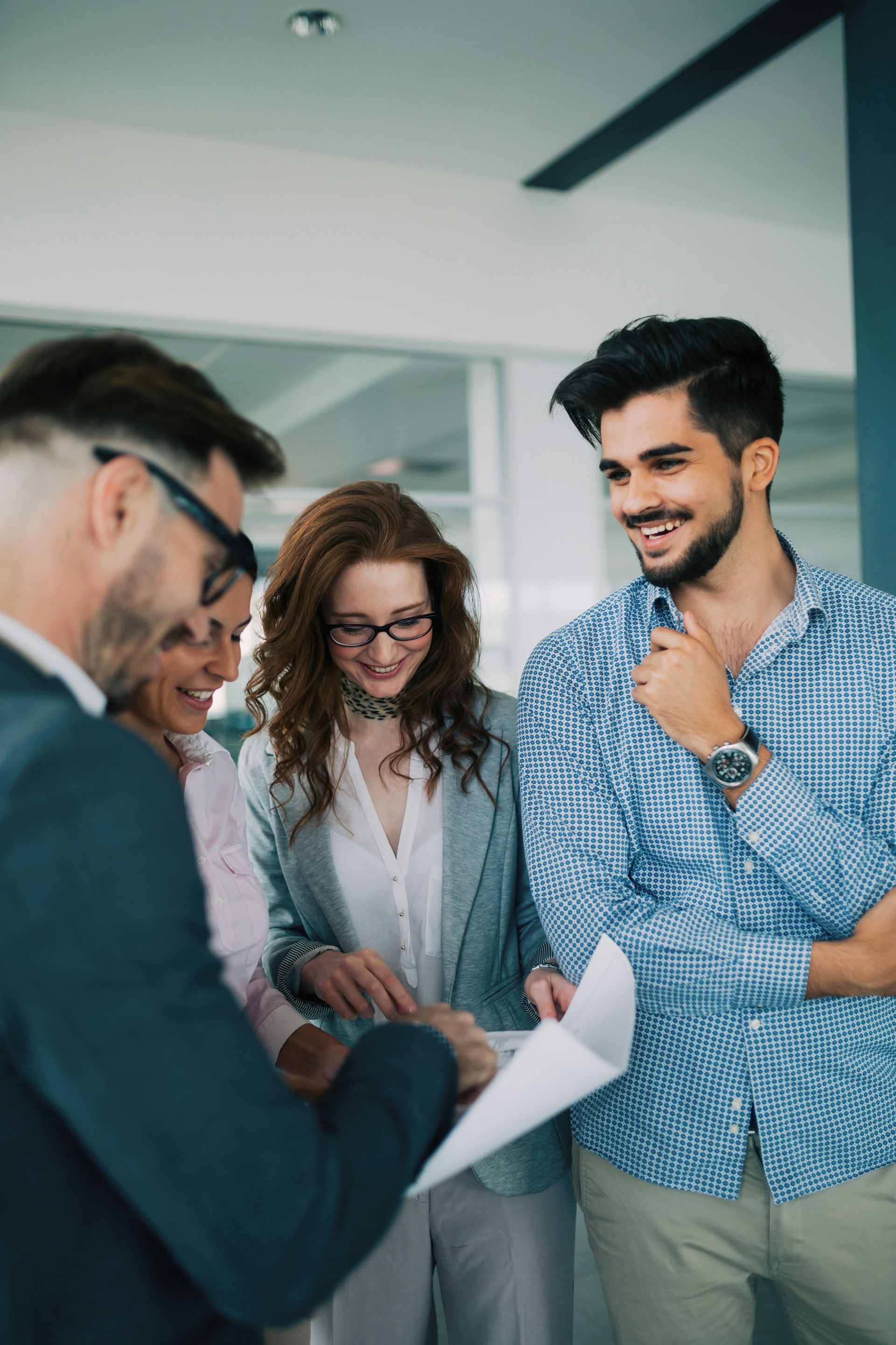 A group of four colleagues in an office setting look at a document together, laughing and smiling.