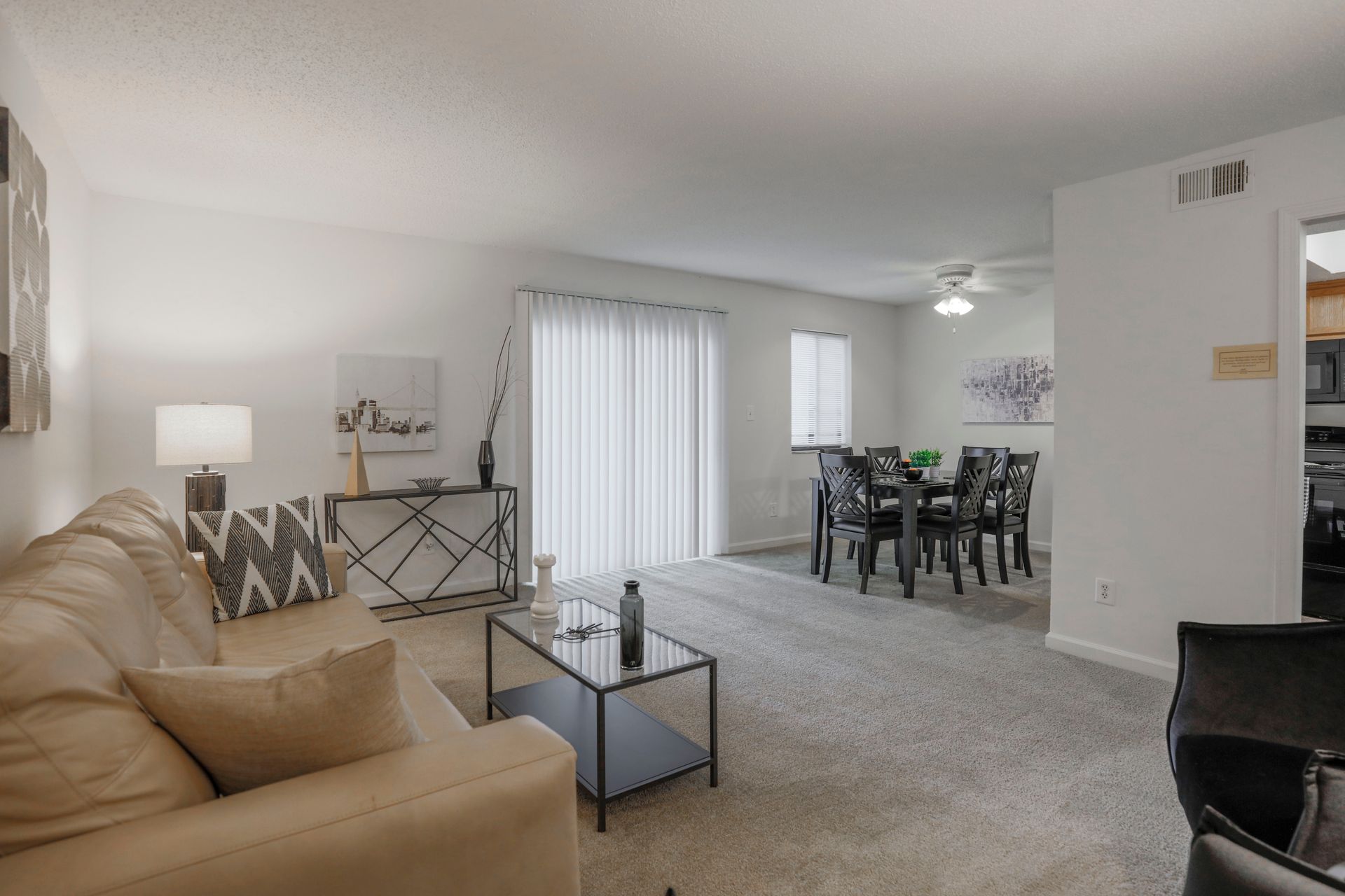 Bright living room with beige sofa, lamp, coffee table, and dining area with sliding glass door.