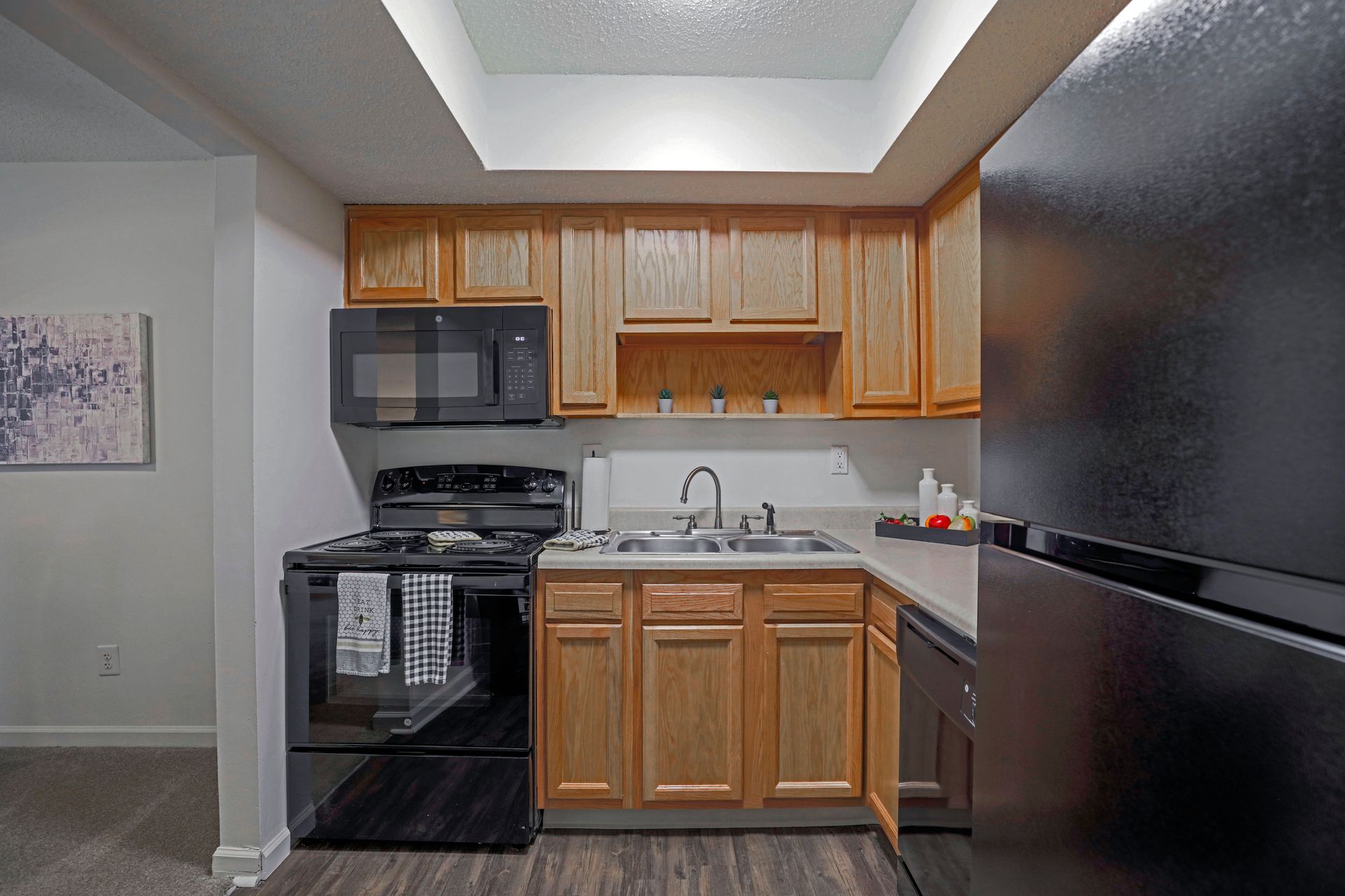 Compact kitchen with black appliances, wood cabinets, and a stainless sink under bright overhead lighting