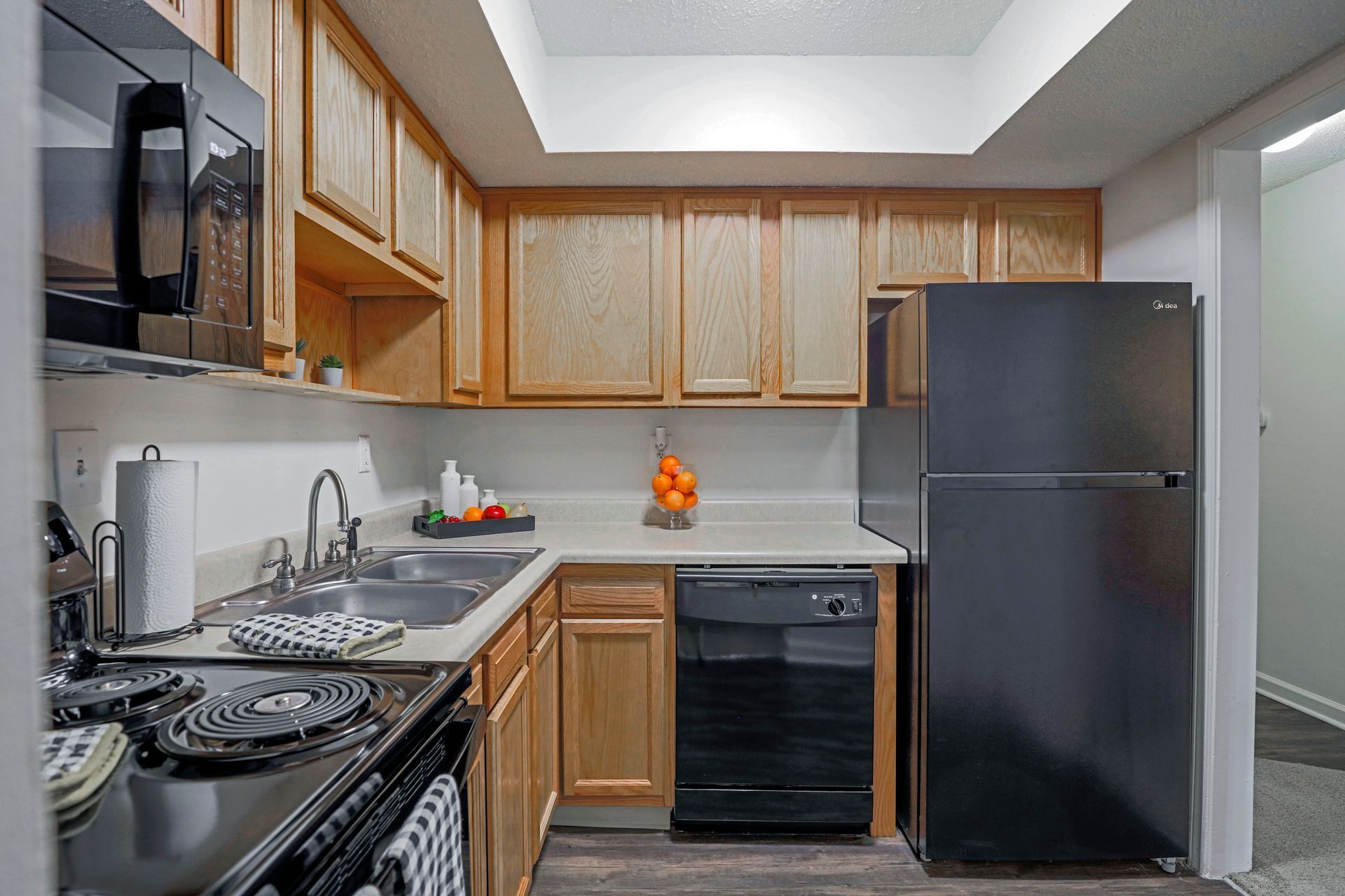 Small kitchen with wood cabinets, black appliances, and a white countertop under bright lighting.