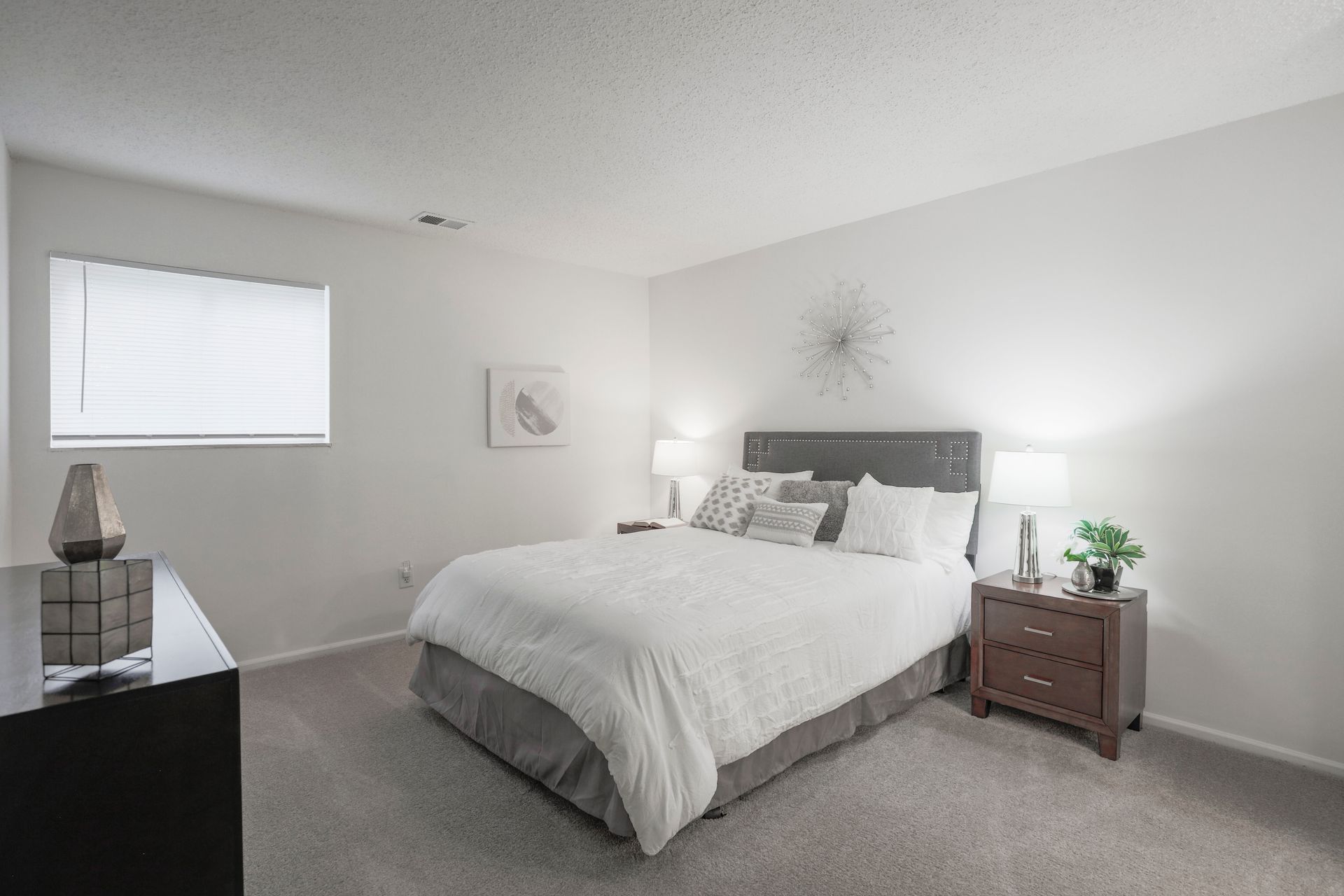 Bright bedroom with a gray tufted bed, white bedding, and nightstands in a neutral room.