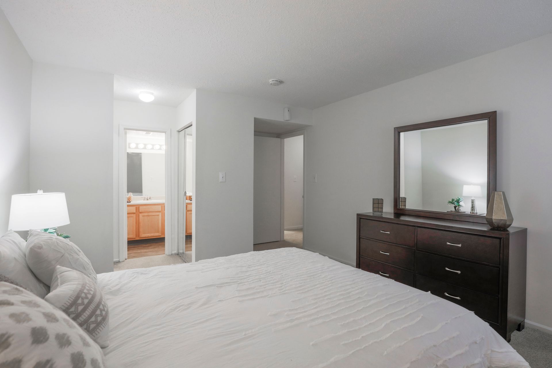 Bright bedroom with a large bed, dresser with mirror, and doorway to a bathroom.