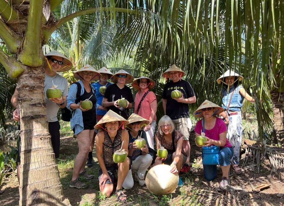 Vacation Travel to Southeast Asia - A group of people are posing for a picture while holding coconuts.