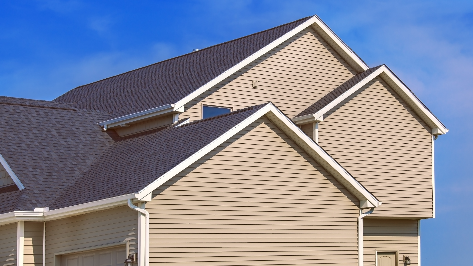 Close-up of beige suburban house exteriors with dark shingled roofs against a blue sky