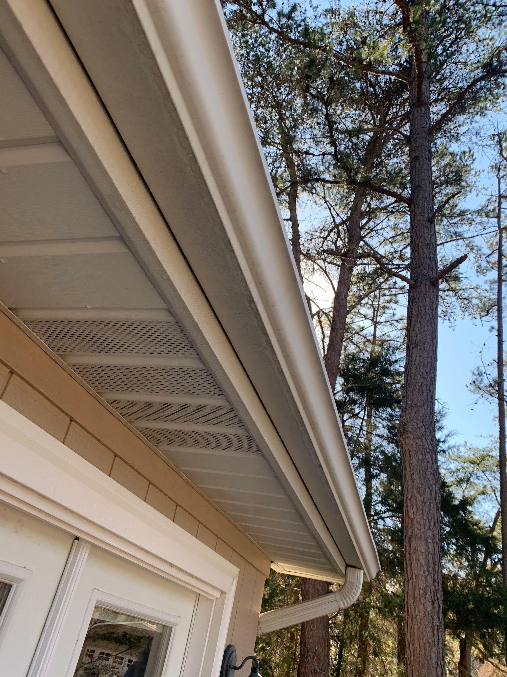 A white gutter on the side of a house with trees in the background.