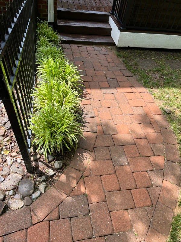 A brick walkway leading to a house with a black fence.