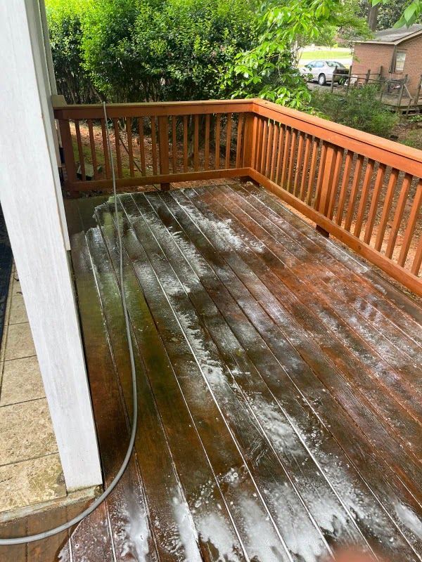 A person is cleaning a wooden deck with a hose.