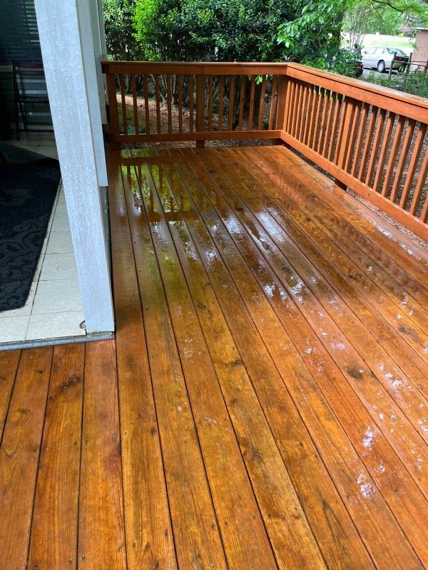 A wooden deck with a railing and a reflection of trees in the water.