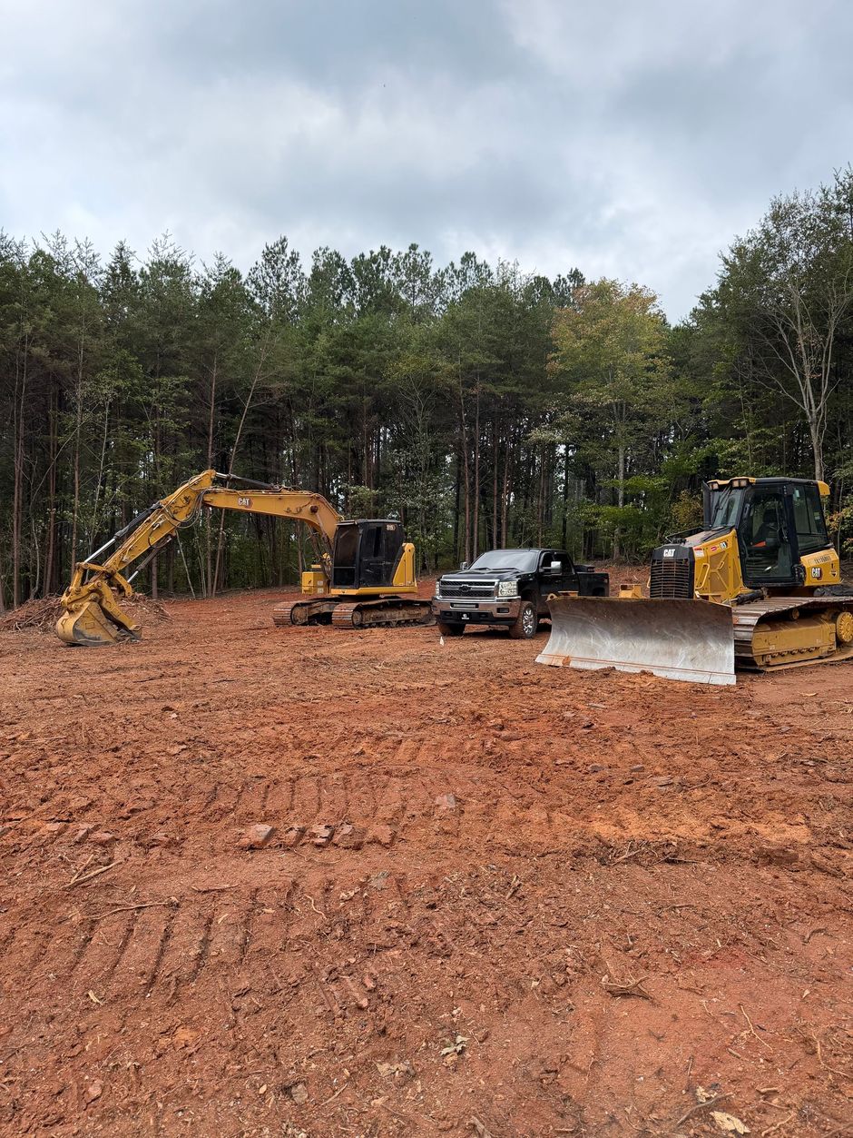 A yellow Caterpillar dozer and excavator lined up with a work truck on a graded piece of property.