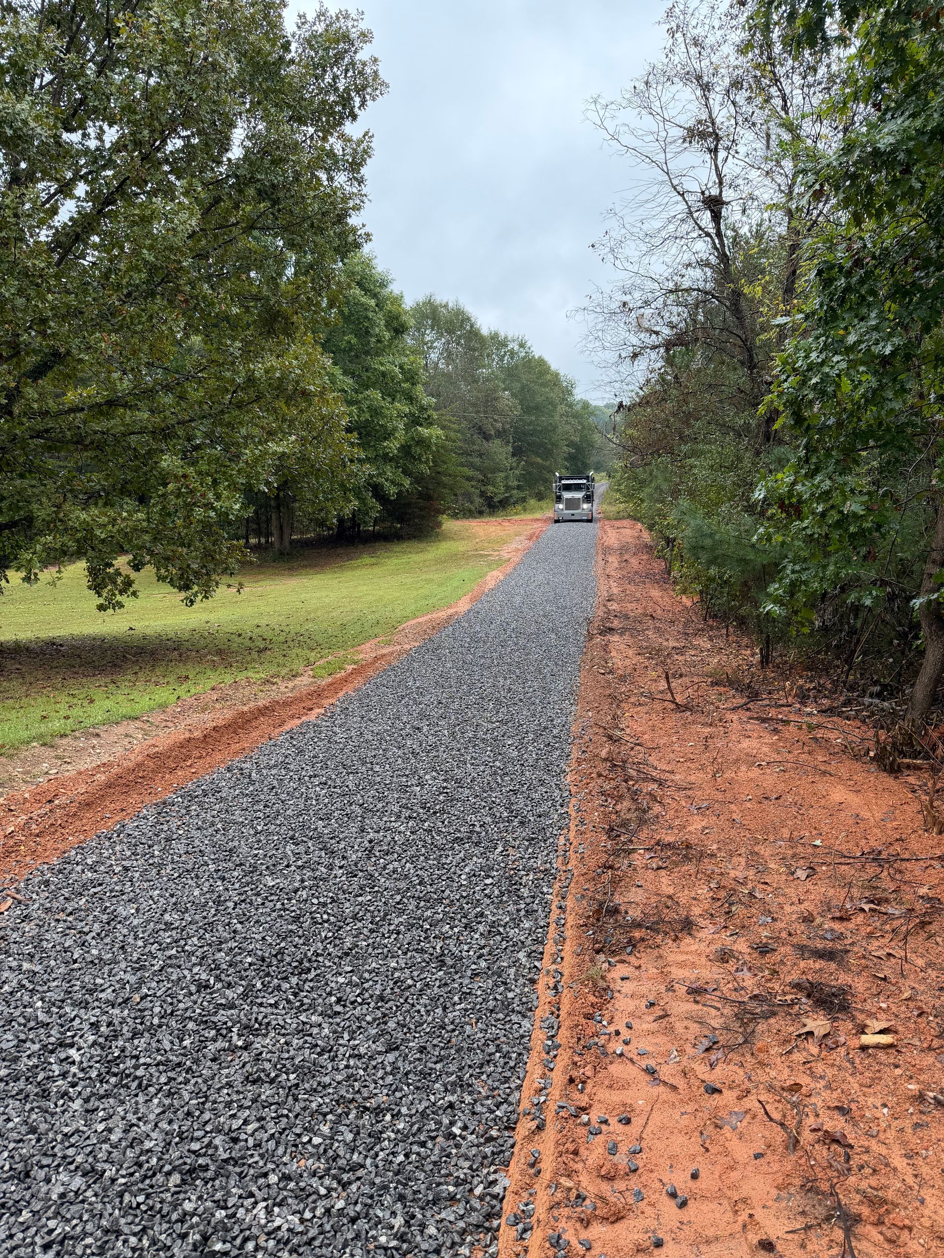 Dump truck unloading gravel onto a freshly graded road.