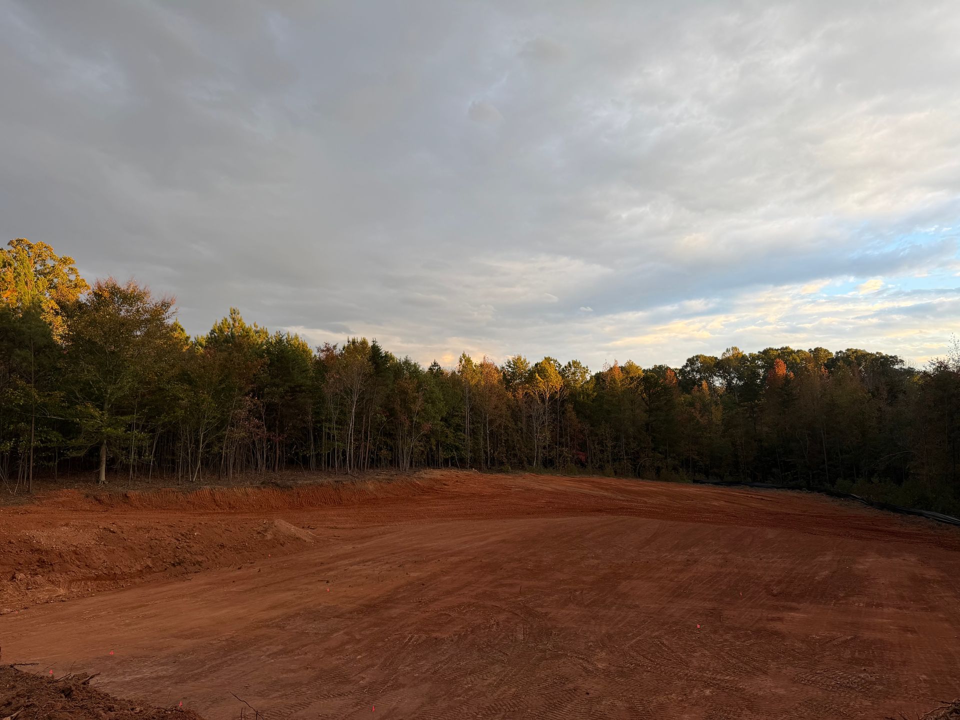 Freshly graded residential basement cut with a backdrop of fall trees and the sun setting.