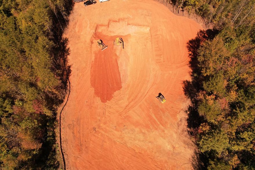 Aerial view of cleared land, red soil, with construction equipment. Edged by green trees.