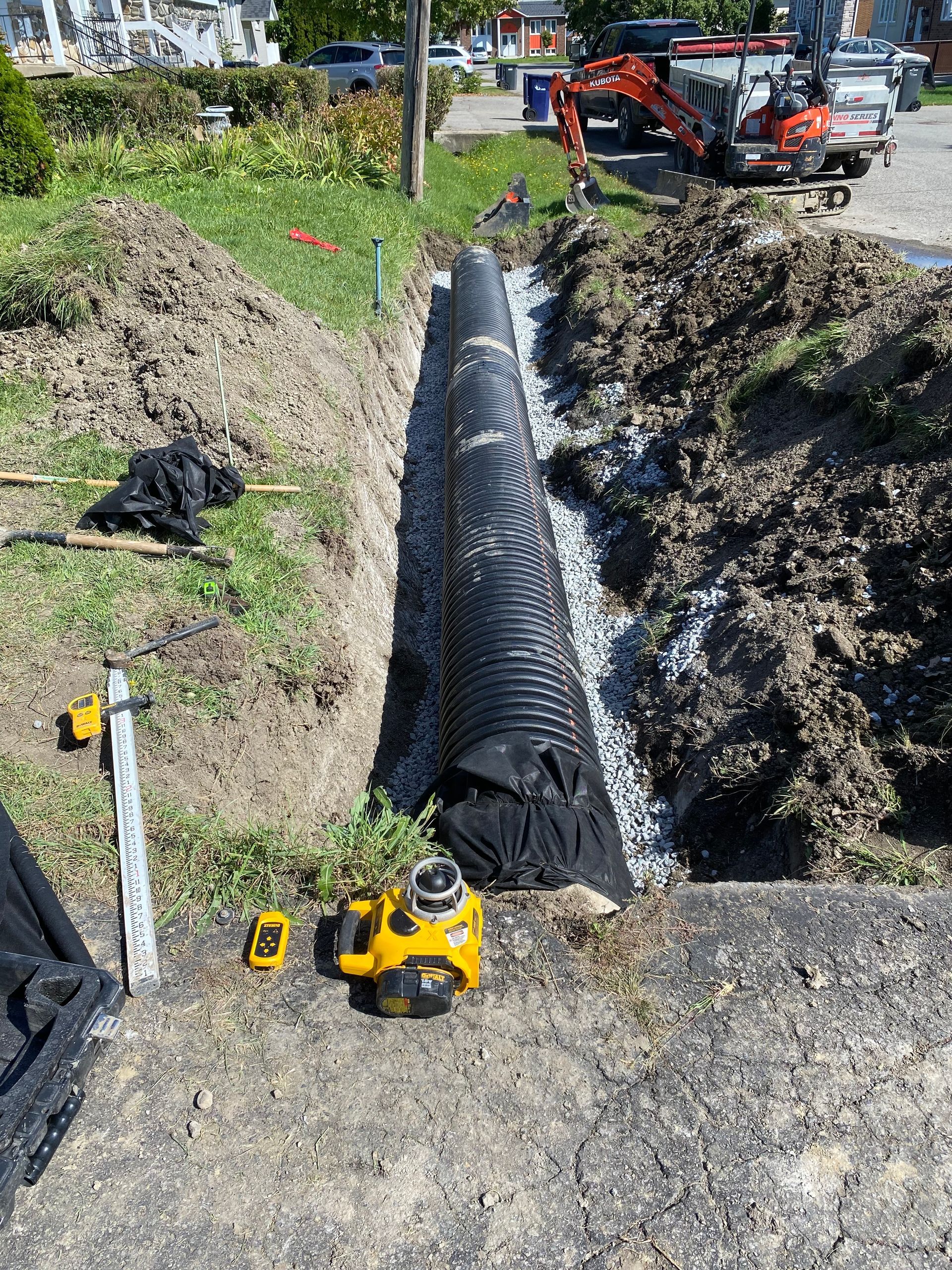 Un gros tuyau est en train d'être installé dans le sol à côté d'un tas de terre.