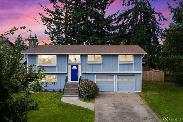 A light blue split-level house with a darker blue accent door, set against a vibrant sunset sky. 