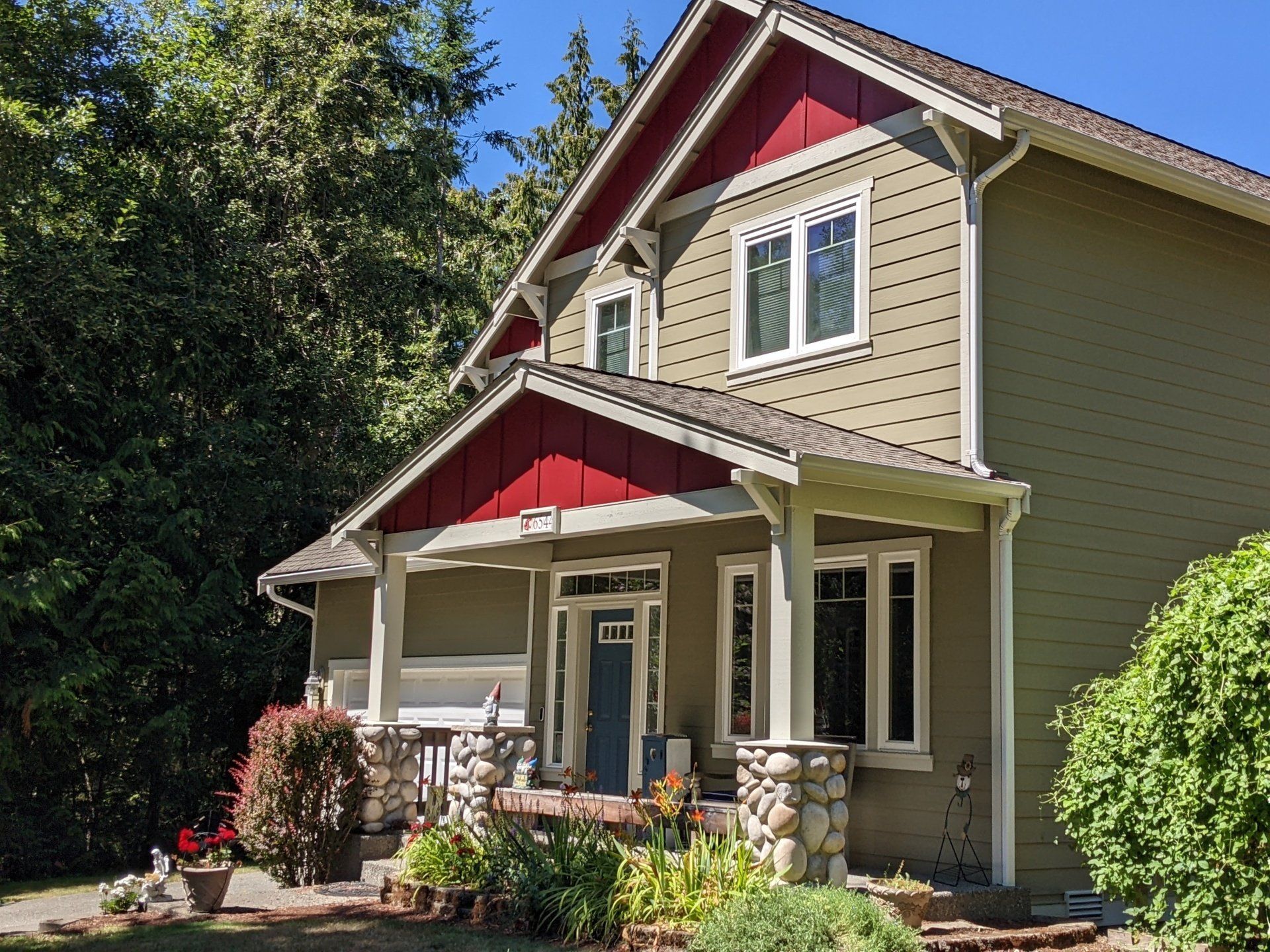 Two‑story home with olive green siding, white trim, and red‑painted gable accents above the porch and upper windows.