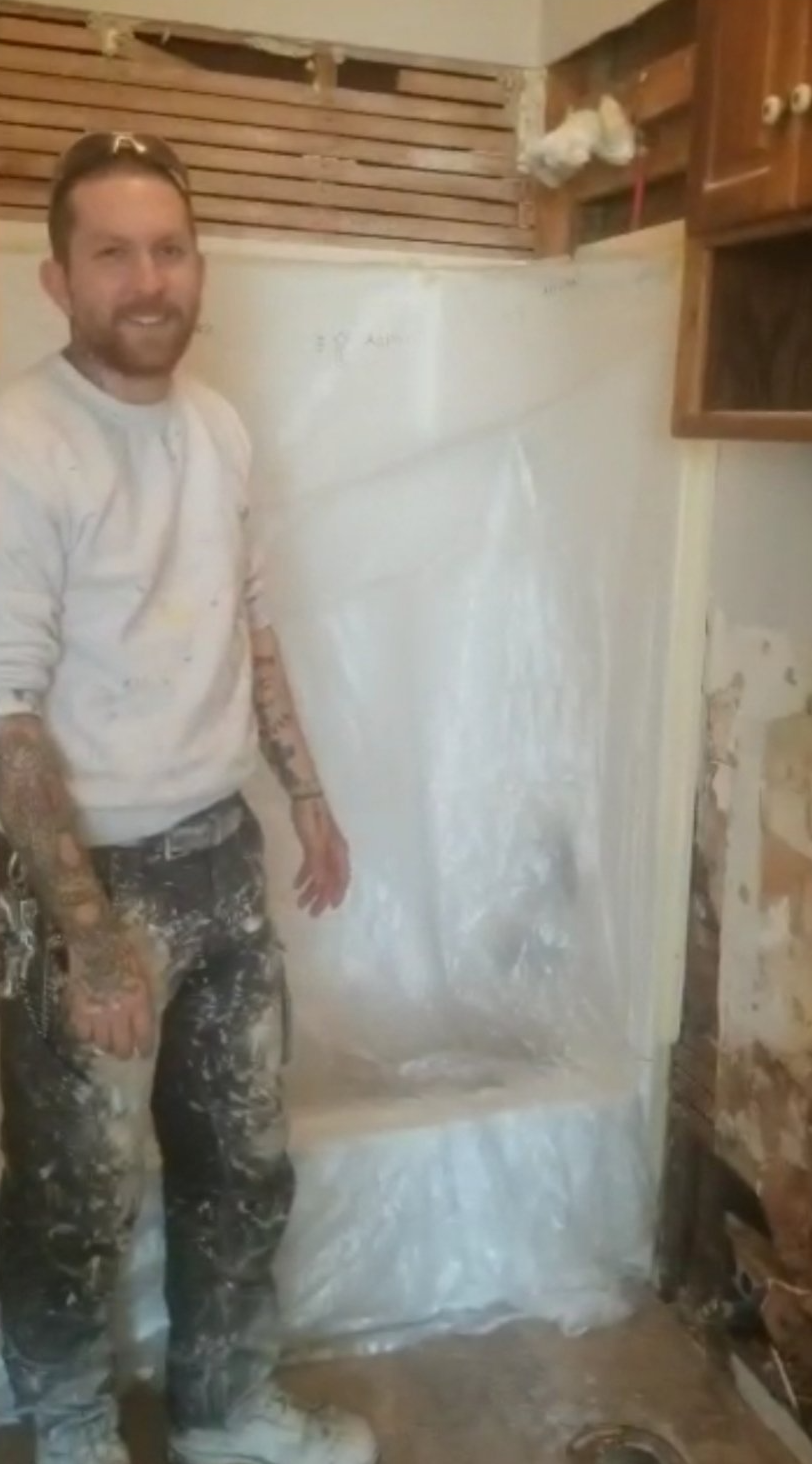 painter standing in bathroom being renovated showing bathtub covered with plastic