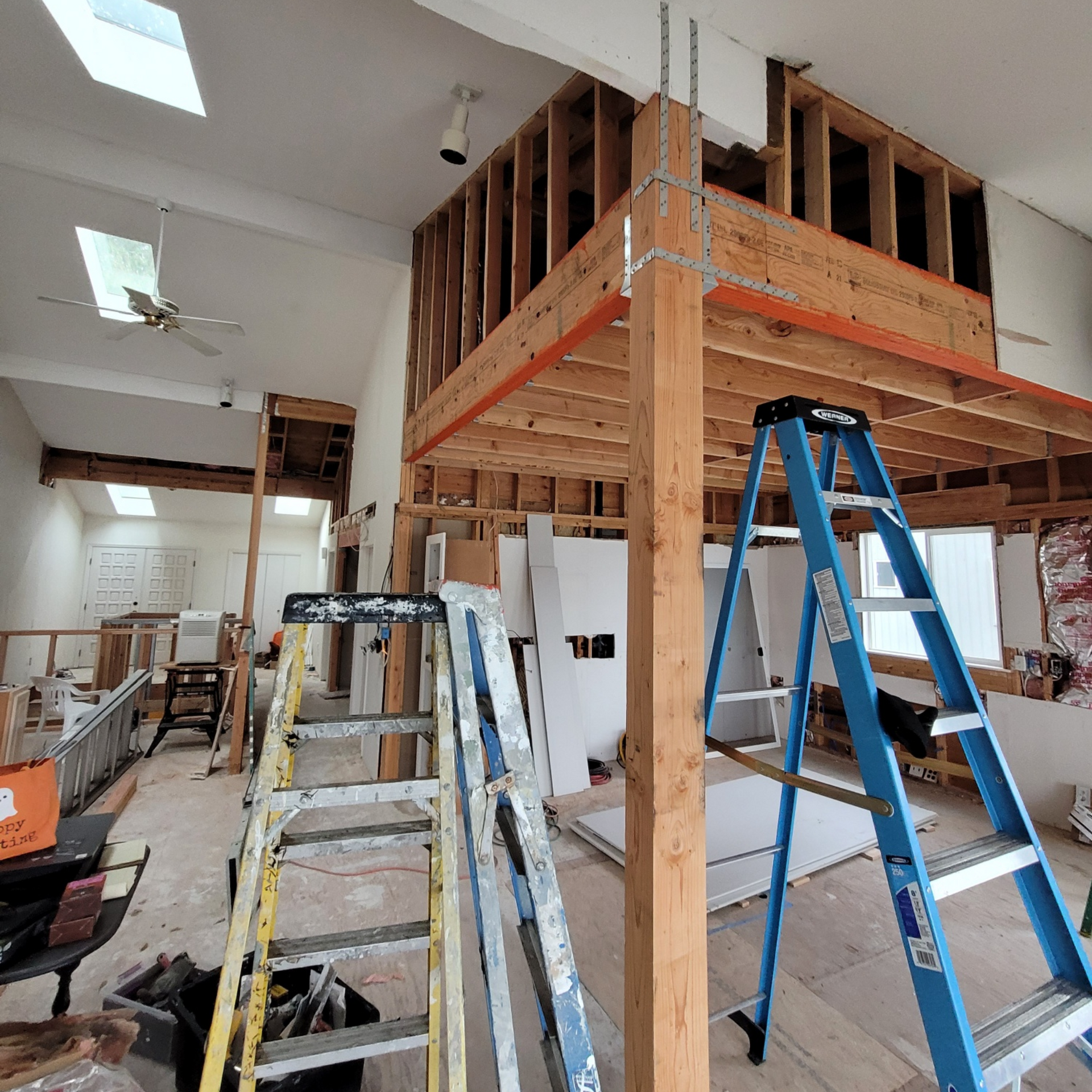 A second-story loft in the process of being built, with work equipment sitting out and most of the drywall still missing.