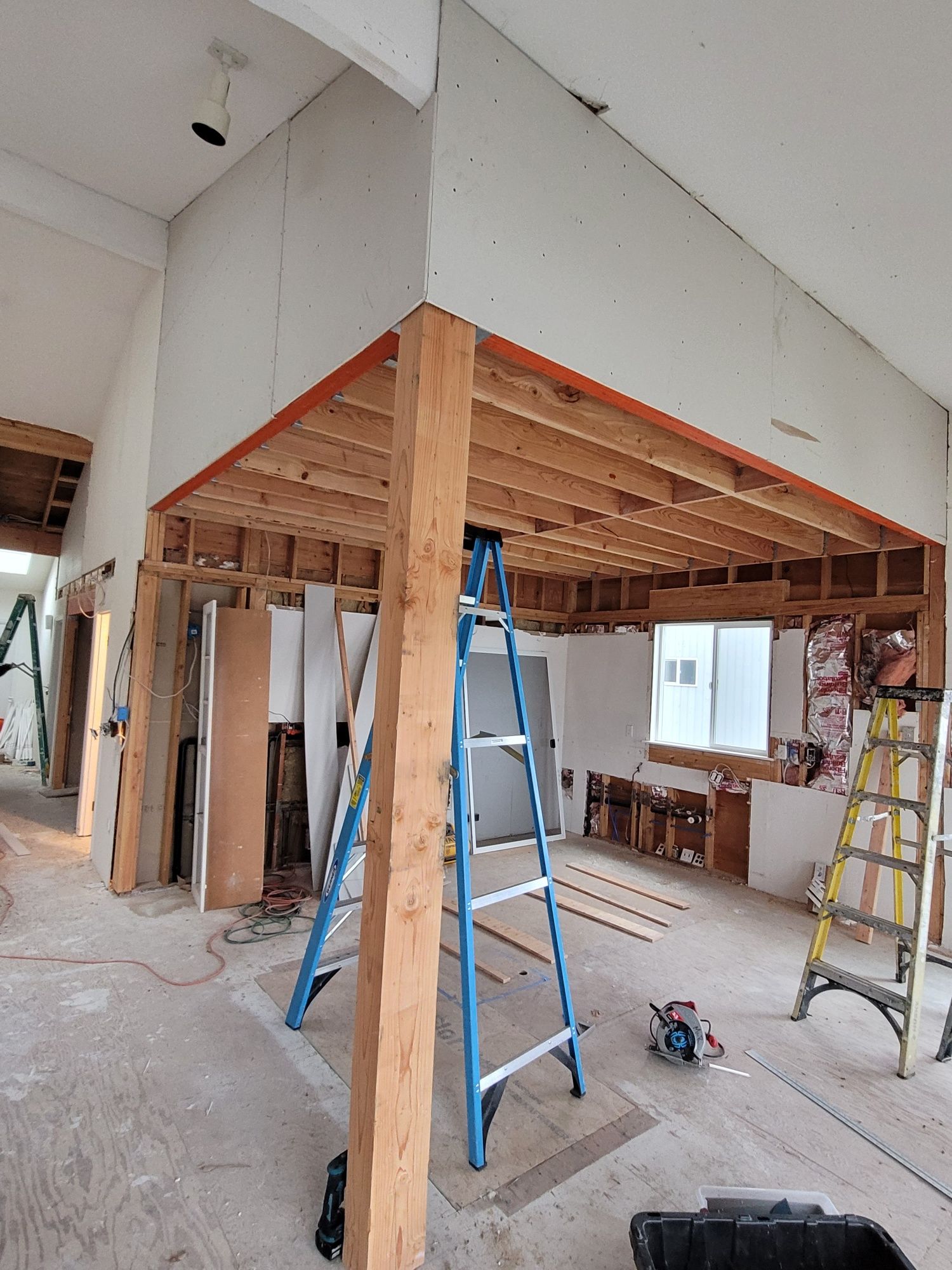 Loft structure under construction with new drywall installed, exposed framing below, and ladders and tools on the floor.