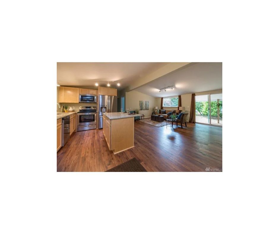 This is an open concept kitchen and living room and dining room area with brown wooded flooring and stainless appliances .