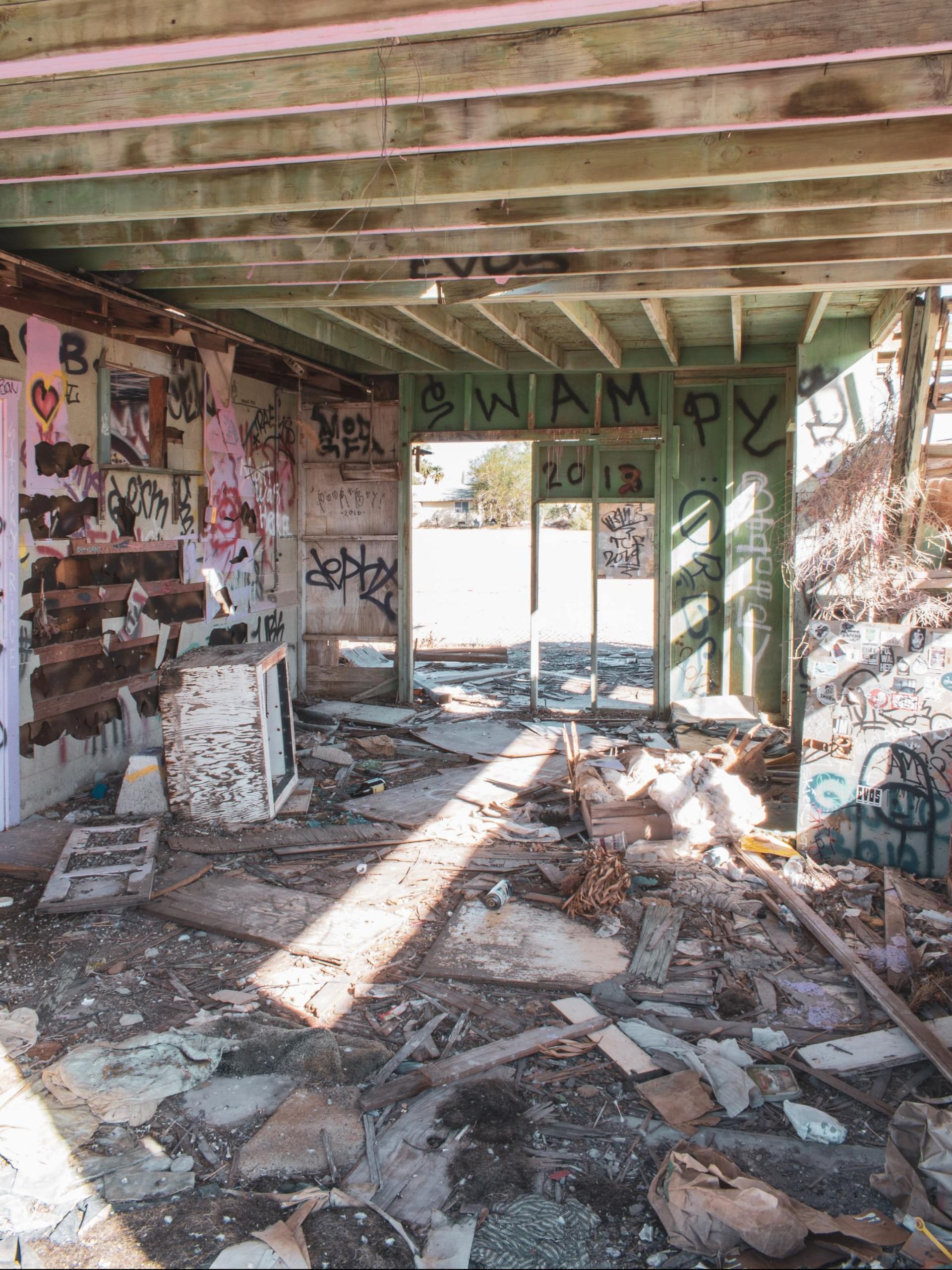 A demolished and graffitied structure with old furnishings and other junk strewn about. 
