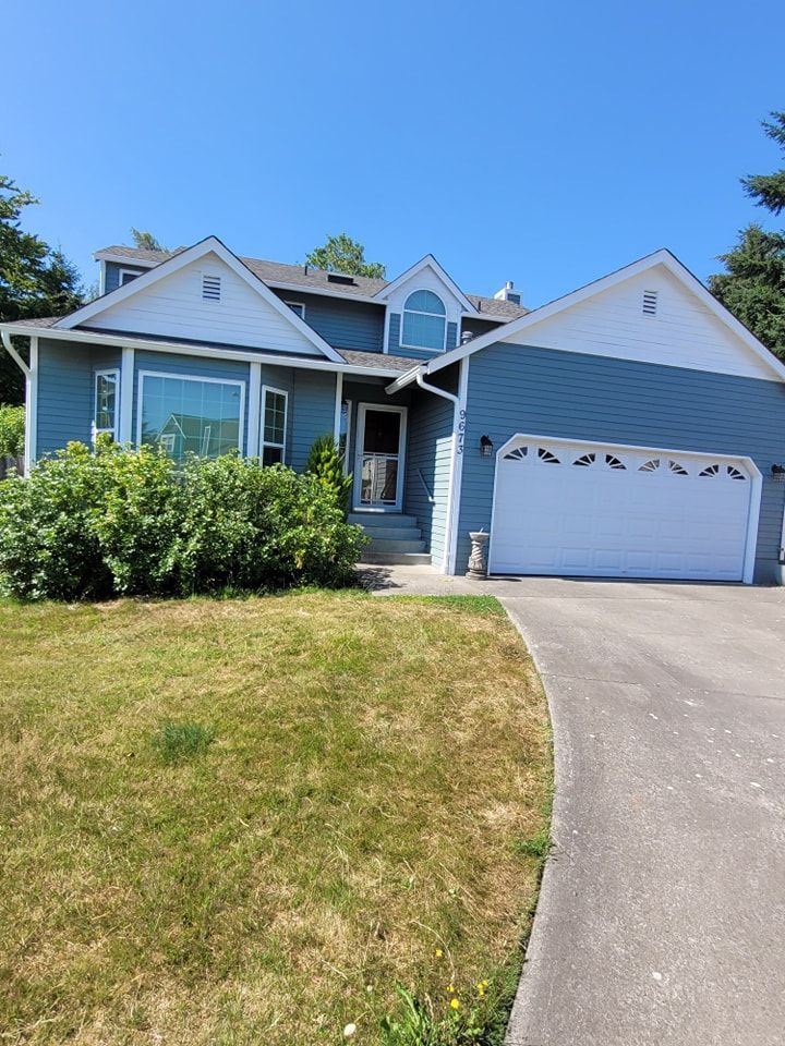 A freshly‑painted blue house with white trim and a white garage door, set on a green lawn with a concrete driveway.