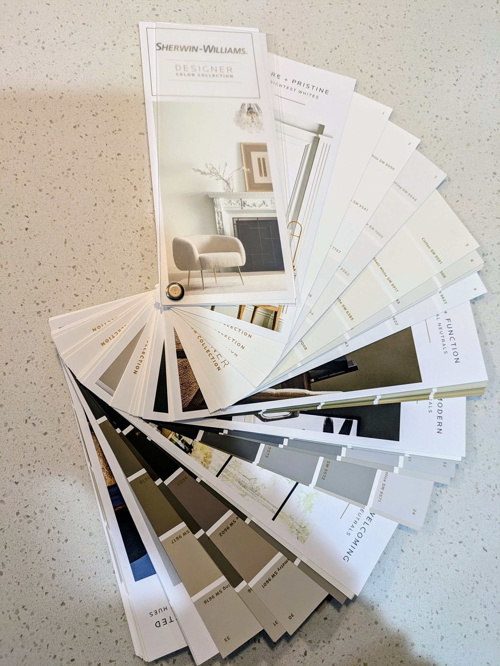 Paint color fan deck fanned out on a white countertop, showcasing various shades of paint for home decor.