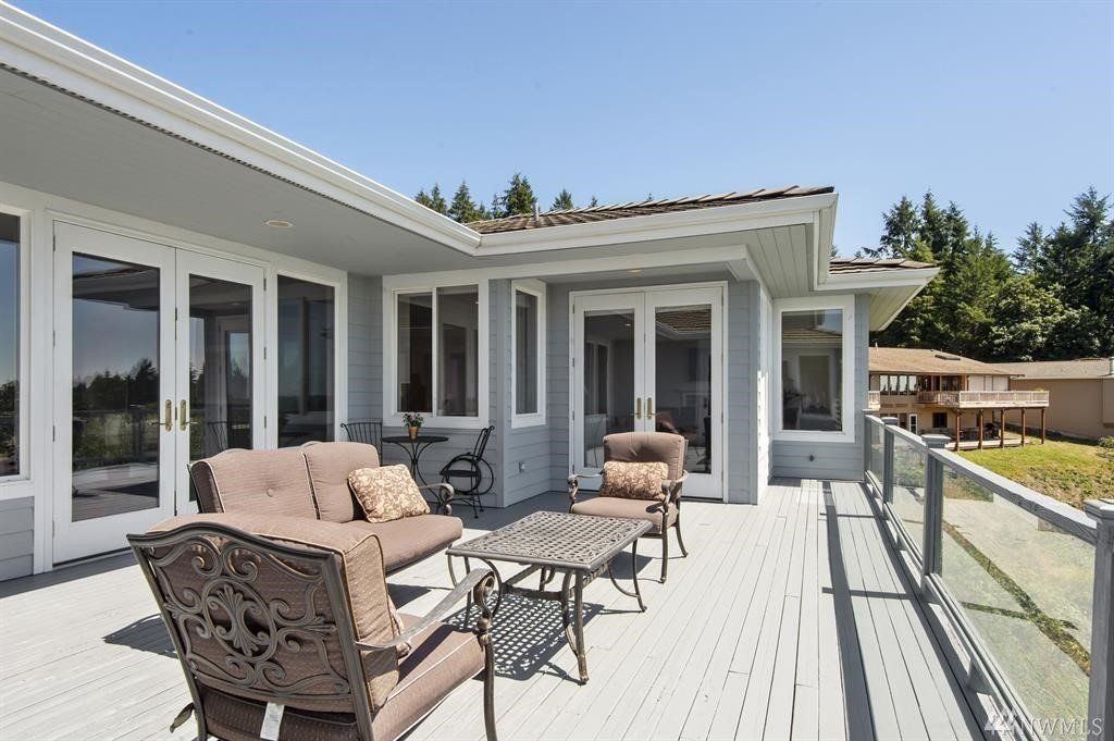 Painted gray deck with glass railing and outdoor seating, overlooking trees and a distant water view.