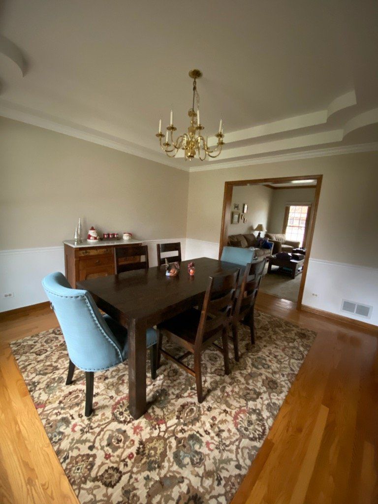 A dining room with fresly-painted cream walls, crown molding a tray ceiling, and a golden chandelier.