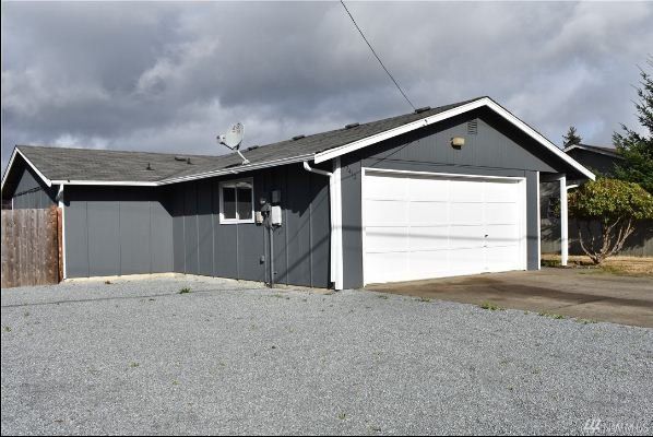 A freshly‑painted gray house with white garage door and gravel driveway.