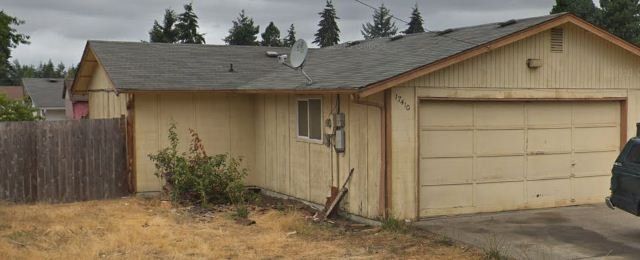 A single‑story beige house with a two‑car garage and a worn exterior paint job.