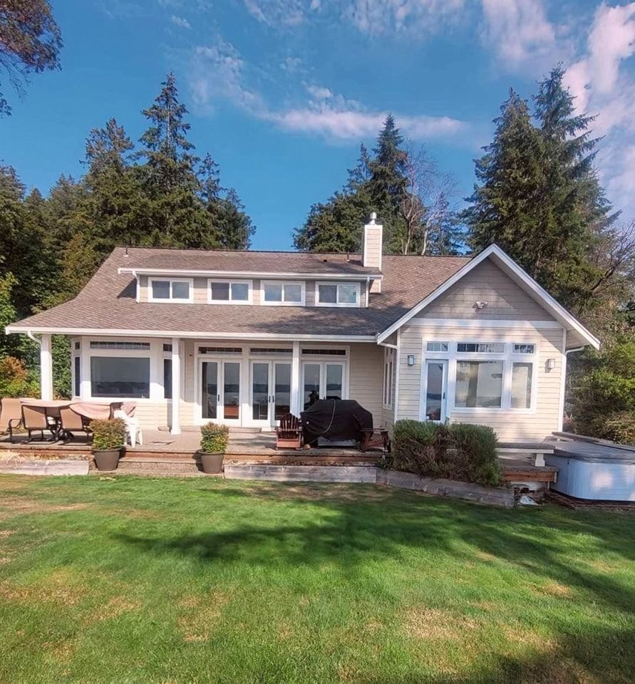 Two‑story home with beige painted exterior, white trim, and stone accents, surrounded by a manicured lawn and driveway.