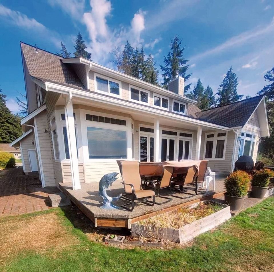 Back view of beige house with patio, grill, seating area, and lawn.