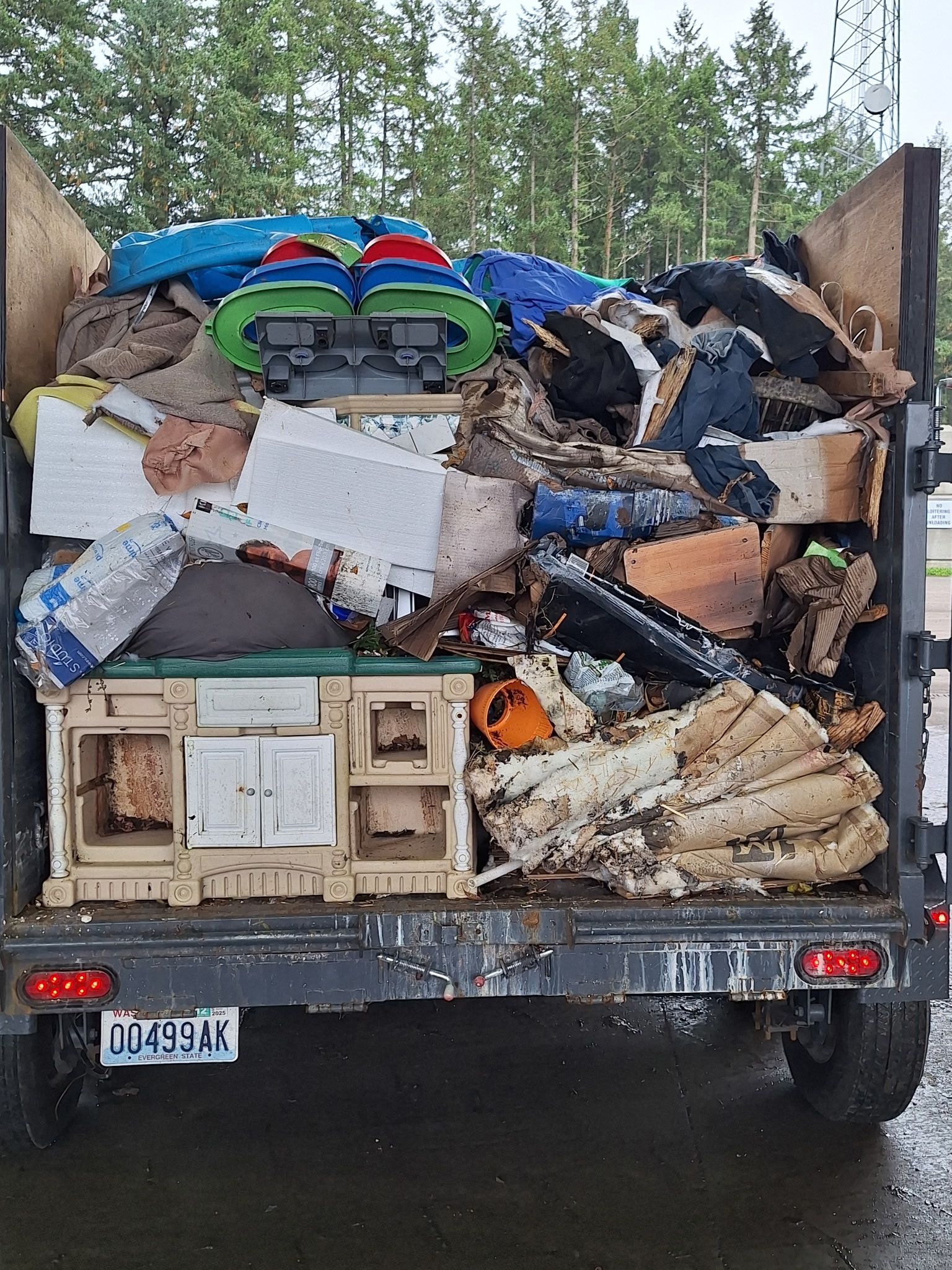 Dump truck bed filled with trash, broken furniture, and debris piled high against the cab.