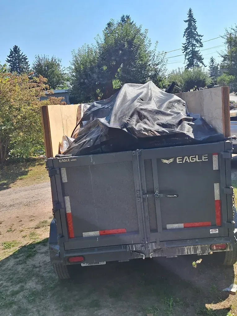 A dumpster trailer is filled, the heap of junk in the trailer covered with a dark blue tarp.