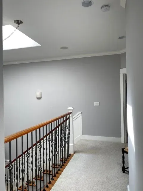 An upstairs view of a hallway and staircase with fresh gray walls and white trim.
