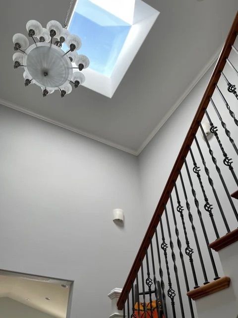 A view from the first floor looking up shows freshly-painted gray walls surrounding a spiral staircase, skylight, and chandelier.