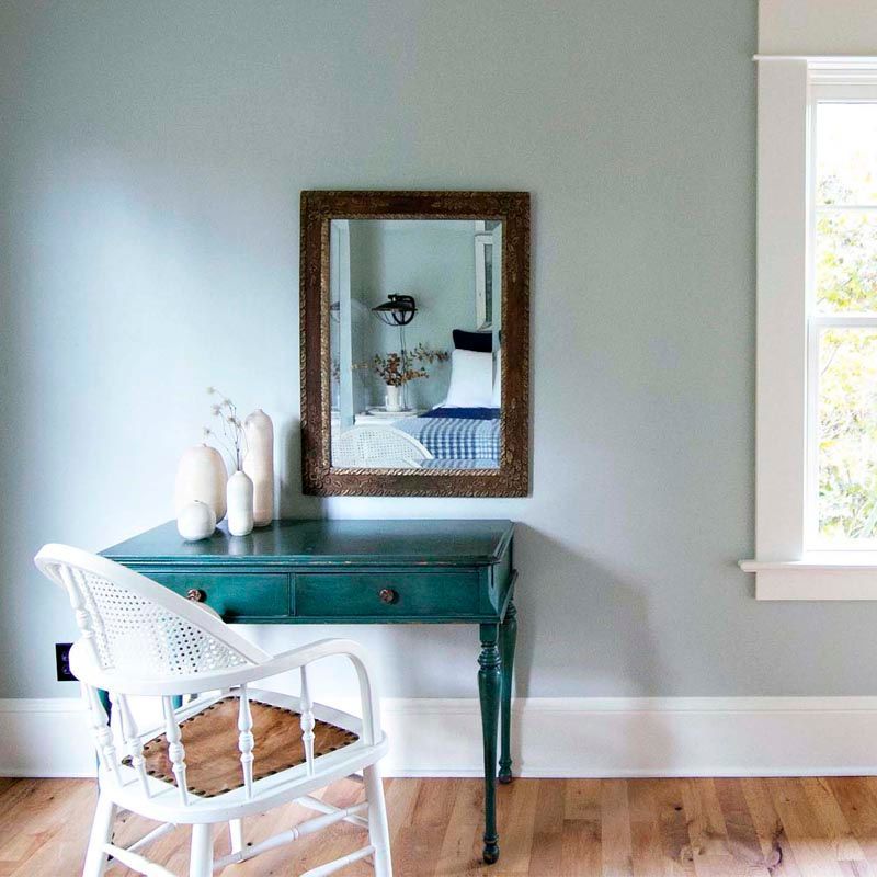 Bright corner with white chair, green desk, mirror, and a blue-gray wall.