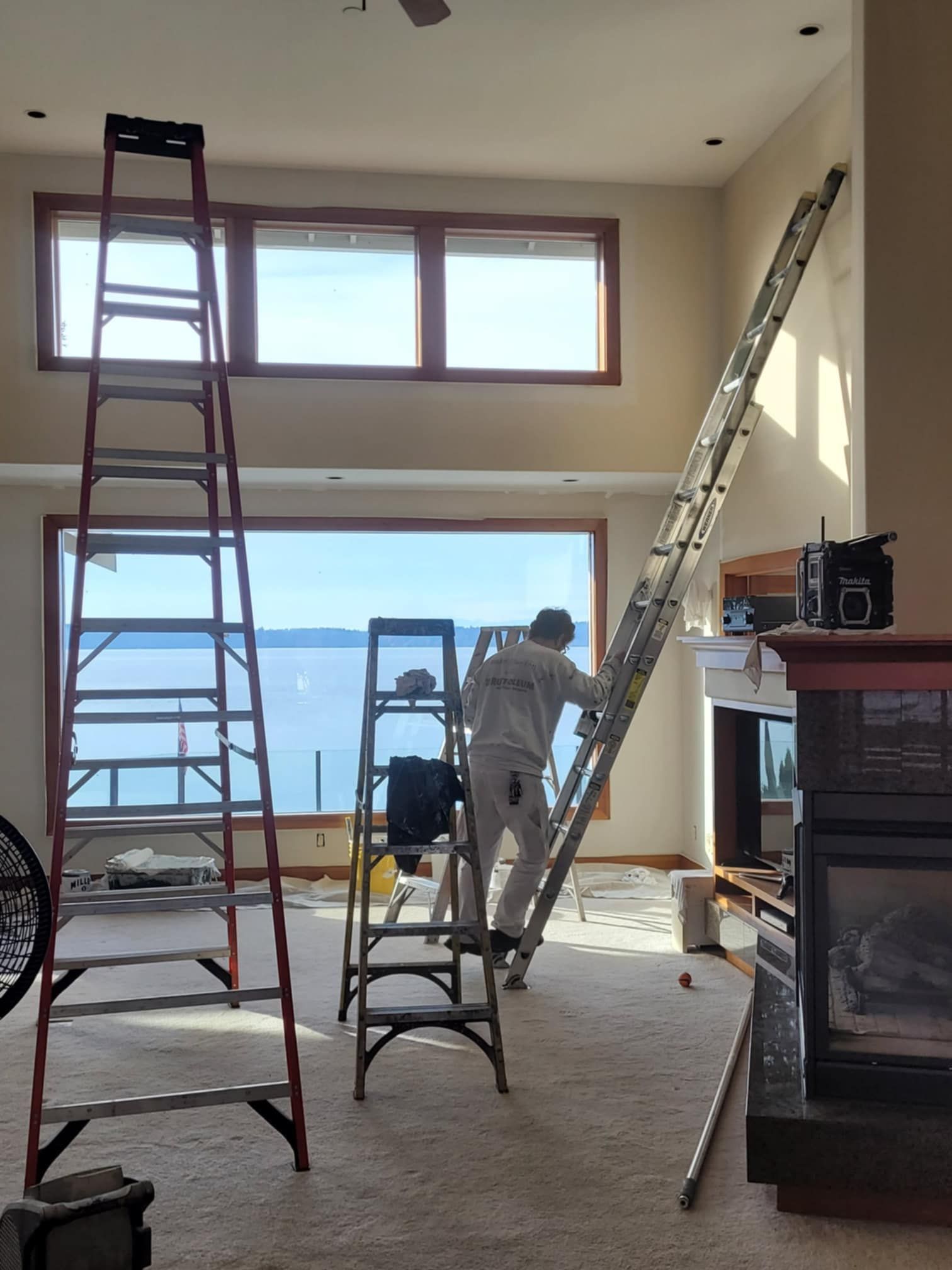 An interior paint job with high ceilings requires multiple extension ladders to be placed around the room in preparation. 