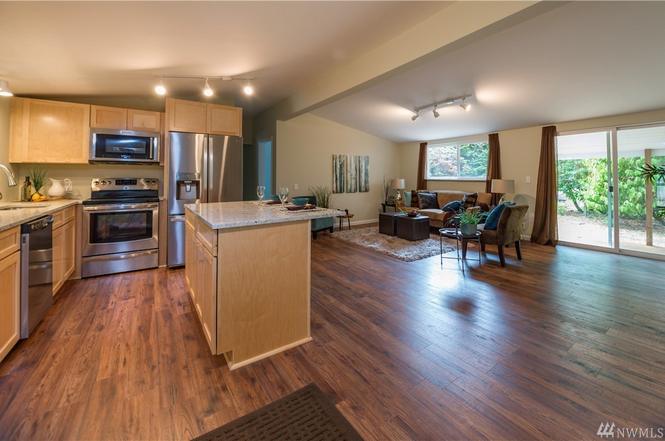 This is an open concept kitchen  and living room and dining room area with brown wooded flooring and stainless appliances .