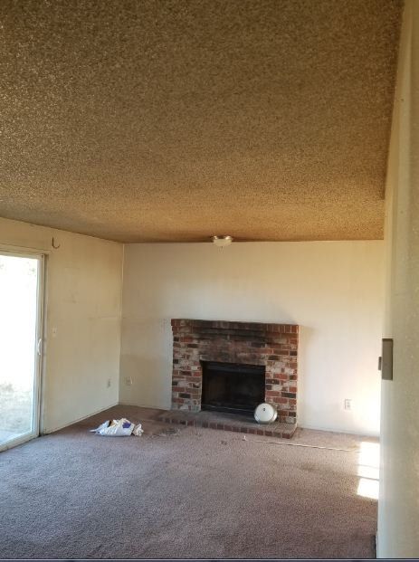 Outdated living room with brick fireplace, sliding glass door, yellowed walls, and stained carpet.