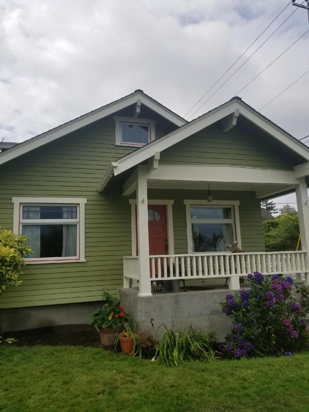 Newly‑painted green Craftsman‑style house with a red front door and a lighter cream colored porch railing and trim.
