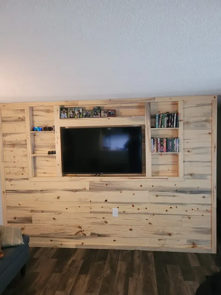 Living room wall finished with natural wood paneling around a mounted TV and built‑in shelves, above a black fireplace unit.