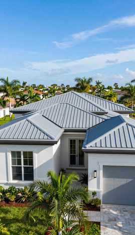 Modern white house with gray metal roof and palm trees under a blue sky