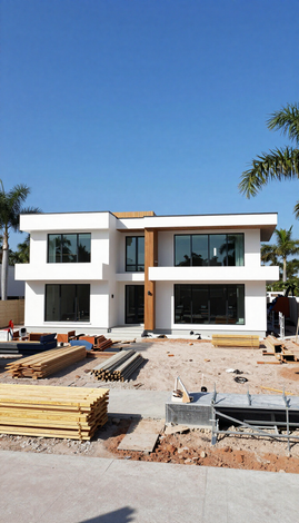 Modern two-story white house under construction with wood stacks and dirt foreground under clear blue sky