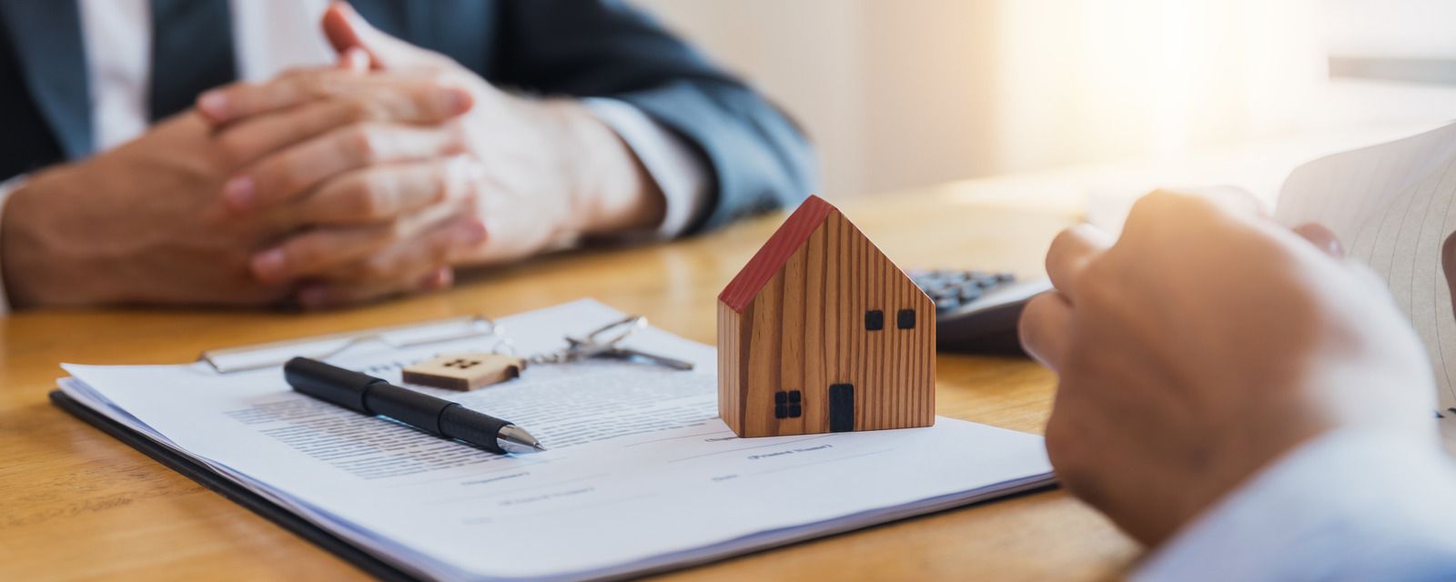 Two people discussing a house model and paperwork at a desk, suggesting a real estate meeting