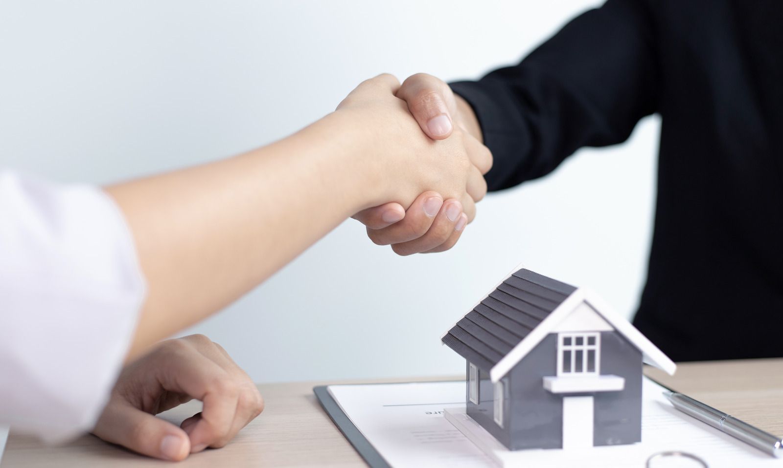 Handshake over a miniature house model on a desk, suggesting a real estate agreement